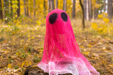 Creative handmade Halloween holiday decoration. pink ghost in autumn leaves forest. Zero waste homemade decor. Mystic placeの写真素材