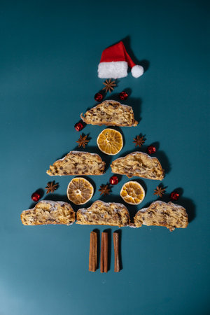 Slices of Christmas Stollen with dried orange cinnamon and decoration Santa hat in shape of Christmas tree. Traditional sweet fruit loaf with icing sugar festive pastry dessert. Holiday baking foodの写真素材