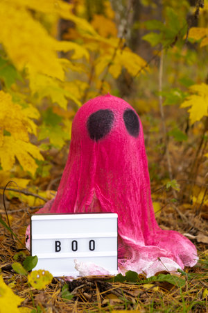 Creative handmade Halloween holiday decoration. pink ghost with Lightbox BOO text in autumn leaves forest. Zero waste homemade decor. Mystic placeの写真素材