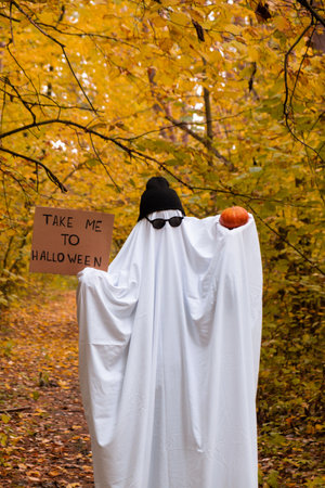 Trendy halloween celebration outdoors in autumn time. Handmade ghost costume from sheets, cap and...