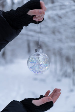 Unrecognizable woman hangs Christmas decoration outdoor in snowy winter forest. Postcard greeting card mock up. Holiday transparent ball toy branch Ornaments New Year celebrationの写真素材