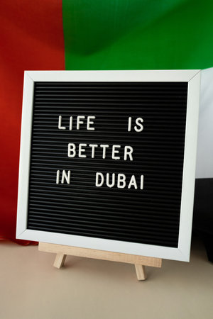 Frame text LIFE IS BETTER IN DUBAI on background of waving UAE flag made from silk. United Arab Emirates flag with concept of tourism and traveling. Inviting greeting card, advertisement. Dubai welcoming cardの写真素材