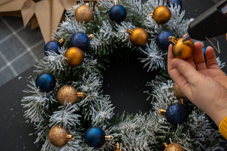 Crafter using hot glue Handmade Christmas wreath from festive blue and yellow decorations. Festive holiday preparation craft master class of creative making decor. Hands-on activities sustainable responsible holiday gift workshopの写真素材