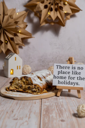Note with saying THERE IS NO PLACE LIKE HOME FOR THE HOLIDAYS.Traditional German Christmas stollen cake in background of handmade festive decor. Winter holiday treats. Vegan baking recipeの写真素材