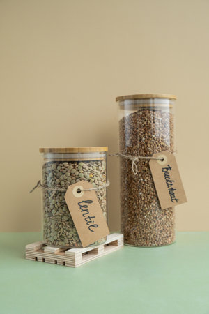 Refillable glass jar with raw buckwheat porridge and green lentil. Copy space Refill product format eco-friendly living. Filling reusable container Whole spelt grain species. High protein fiber-rich vegan plant based food ingredient. Gluten free healthy nutritional dietaryの写真素材
