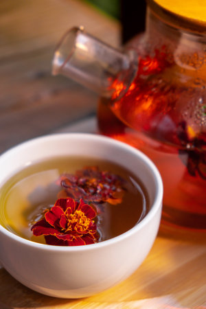 Marigold flower tea in glass mug with tea pot on garden table. Herbal tea with fresh yellow blossom flowers tea cup. Green clearing infusion Wildflowersの写真素材