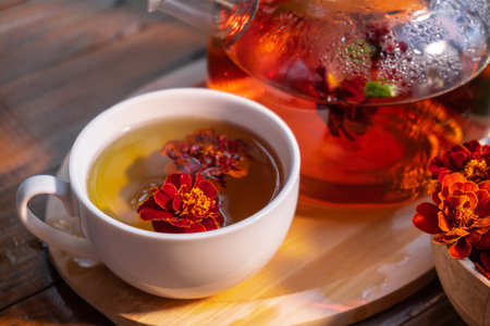 Marigold tea still life on table in green garden background. Healthy hot drink benefits. Natural organic aromatic drink in cup. Home-grown immunity-boosting herbs for tea. Autumn winter warming drinkの写真素材