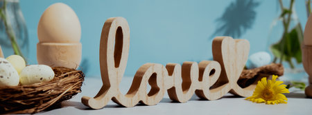 Wooden word LOVE traditional greeting to christian holiday. Festive mood composition with bunnies and yellow flowers on pastel blue background. Sustainable natural materialsの写真素材