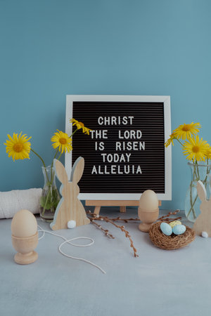 CHRIST THE LORD IS RISEN TODAY ALLELUIA text on letter board with bunny wooden figures eggs and fresh flowers. Easter composition content still life. Symbols of springの写真素材