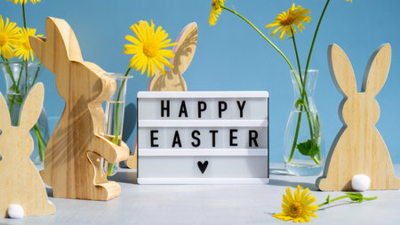 Lightbox with message HAPPY EASTER on festive blue background and eco-friendly zero waste natural decoration. Yellow daisies flowers. Holidayの写真素材