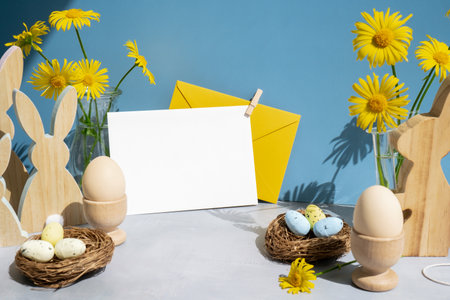 Empty white envelope mock up postcard copy space on festive blue background and eco-friendly zero waste natural decoration. Yellow daisies flowers. Bunny egg. Holidayの写真素材