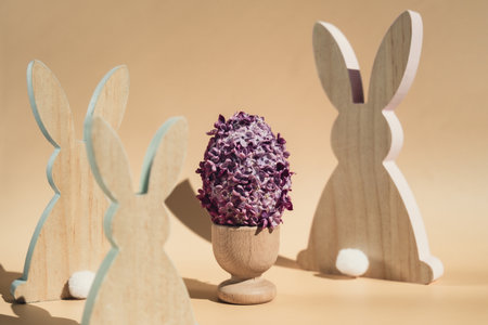 Wooden minimalism low-key bunny decor. Easter egg made of lilac spring flowers in pastel beige background. Sustainable holiday minimalistic still life composition. Copy space template for invitation greeting cardの写真素材