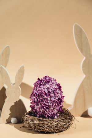 Wooden minimalism low-key bunny decor. Easter egg made of lilac spring flowers in pastel beige background. Sustainable holiday minimalistic still life composition. Copy space template for invitation greeting cardの写真素材