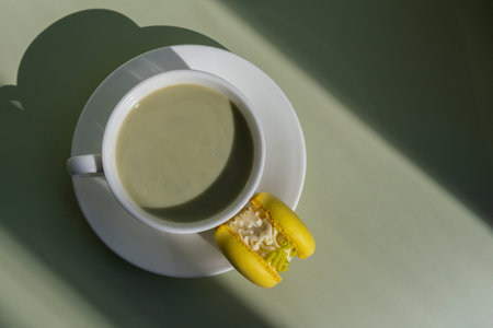 Green latte matcha with yellow macaron dessert on pastel background with creative deep shadows. Concept of holiday breakfast morning tea drink. Cozy minimalist superfood vibrant colors healthy eating. Organic caffeine-freeの写真素材