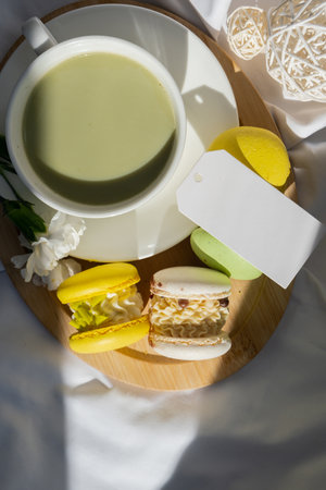 Empty message paper note copy space Nutrient-rich matcha drink with trendy macaron dessert on wooden tray in bed with fresh flowers. Morning beautiful breakfast present gift idea. Vibrant creative colors. Natural energy giversの写真素材