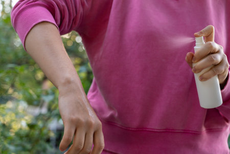 Person spraying insect repellent at her hand outdoors during summer. Trying to kill mosquitoes and...