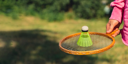 Female hand holding Neon yellow badminton shuttlecock and wooden racket outdoors. Copy space soft selective focus on shuttlecocks. Alternative fitness recreationalの写真素材