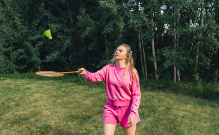 Pretty young woman play with Neon yellow badminton shuttlecock and racket on green grass outdoors. Alternative fitness recreationalの写真素材