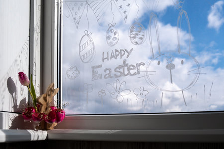 HAPPY EASTER text on creative painted window with white marker. Easter bunny rabbit decoration on big clear window. Springtime idea home decorationの写真素材