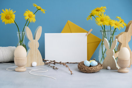 Empty white envelope mock up postcard copy space on festive blue background and eco-friendly zero waste natural decoration. Yellow daisies flowers. Bunny egg. Holidayの写真素材
