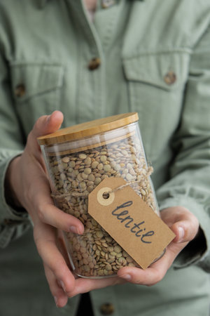 Woman holding Raw green lentil in sustainable natural packaging. Refillable glass jar. Gluten free cereals. Health gut benefits. Concept of alternative whole spelt grain ingredient. Vegetarian diet recipes. Plant-based lifestyle. Protein richの写真素材
