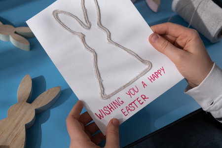 Person holding handmade greeting card with message WISHING YOU HAPPY EASTER written in beautiful handwriting. Gesture shows excitement and joy for the upcoming event. Springtime holiday gift present zero cost ideas. Creative artの写真素材