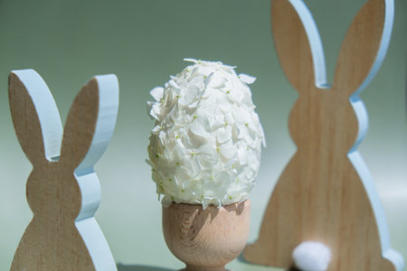 Wooden minimalism low-key bunny decor. Easter egg made of white lilac spring flowers in pastel green background. Sustainable holiday minimalistic still life composition. Copy space template for invitation greeting cardの写真素材
