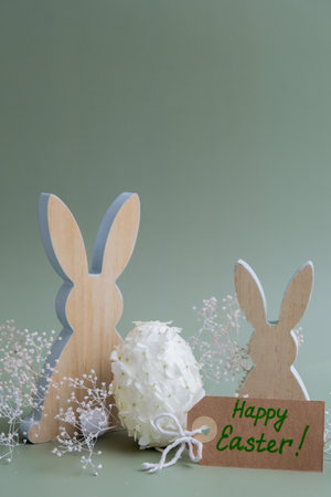 HAPPY EASTER paper note Wooden minimalism low-key bunny decor. Easter egg made of white lilac spring flowers in pastel green background. Sustainable holiday minimalistic still life composition. Wishes greeting cardの写真素材