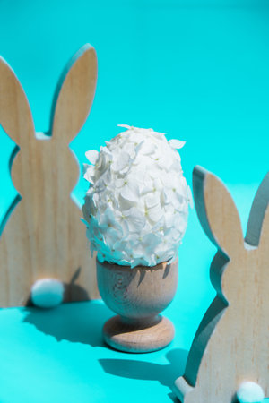 Creative Easter egg shape made of white lilac spring petals flowers. Responsible holidays decoration wooden rabbit bunny decor. Minimal holiday concept still life. Copy spaceの写真素材