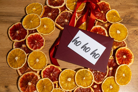 Christmas handmade wreath made of dried slices of orange and grapefruit with red envelope and paper note with HO HO HO text. Winter holiday celebration greeting cardの写真素材