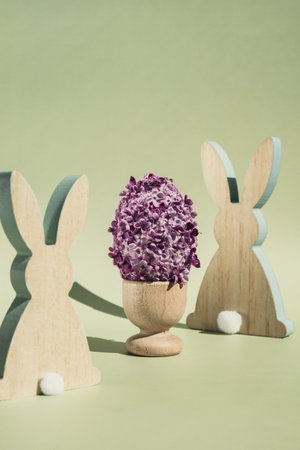 Creative Easter egg shape made of lilac spring petals flowers. Eco-friendly wooden bunnies decoration. Minimal holiday concept still life. Copy space greeting cardの写真素材