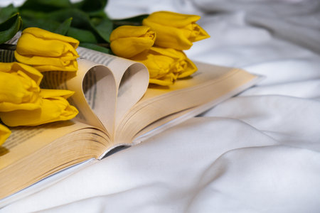 Book pages in shape of heart symbol love with bouquet of pink tulips on messy bed. Romantic morning scene. Greeting card Holiday flowers springtimeの写真素材