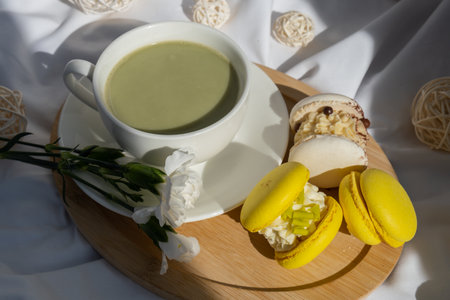 Sweet yellow macaron dessert. Cup of green plant based matcha tea latte in cozy morning atmosphere. Creative holiday romantic idea. Herbal prebiotic fiber superfood beverage antioxidant-rich immunity-boostingの写真素材