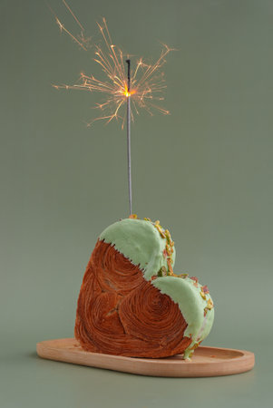 Shiny festive candle sparkler birthday celebration holiday Delightful and vibrant heartshaped pastry croissant treat, beautifully topped with colorful frosting nut galore. Mock up template copy space. Food experimentation viral dessert creativeの写真素材