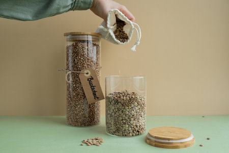 Unrecognizable woman refill Refillable glass jar with raw buckwheat and green lentil porridge in cotton bag. Product format eco-friendly living. Filling reusable container Whole spelt grain species. High protein fiber-rich vegan plant based food ingredient. Gluten free superfood healthy nutritional dietaryの写真素材