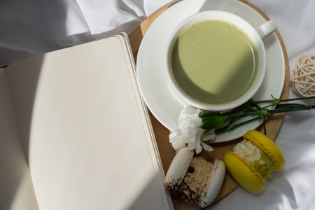 Green latte matcha sweet macaron and empty notebook self reflection journal on bed. Concept of holiday breakfast morning tea drink. Cozy minimalist superfood vibrant colors healthy eating. Organic caffeine-freeの写真素材
