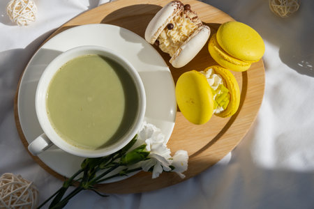 Sweet yellow macaron dessert. Cup of green plant based matcha tea latte in cozy morning atmosphere. Creative holiday romantic idea. Herbal prebiotic fiber superfood beverage antioxidant-rich immunity-boostingの写真素材