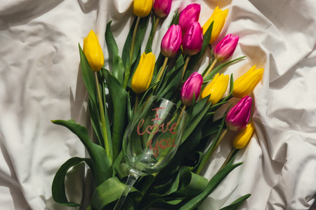 Wine glass with words I LOVE YOU Fresh bouquet of colorful tulip flowers on bed. Gift present idea for holiday birthday 8 March Mothers Day Valentines dayの写真素材