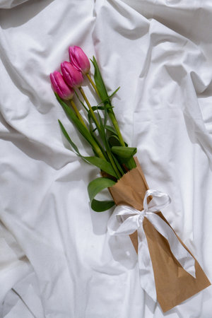 Bouquet of pink tulips in craft eco-friendly paper bag on bed. Romantic morning scene. Greeting card Holiday flowers springtimeの写真素材