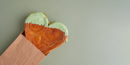 Heart shaped pistachio croissant delivery take away to go food on green background with copy space. Puff pastry trendy sweet dessert bakery. Creamy dough experimentの写真素材