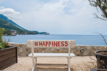 White wooden bench with hashtag HAPPINESS word and view on seacoast near Budva Montenegro. Beautiful turquoise sea and green mountains. Concept of balance slowing down peace took yourself out of the rush. Wellbeing digital detoxの写真素材