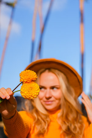 Woman in yellow sweater close her eyes with yellow dahlia Selective focus Bush of autumnal orange...