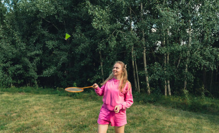Pretty young woman play with Neon yellow badminton shuttlecock and racket on green grass outdoors....