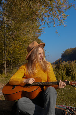 Portrait of smiling caucasian artist plays wooden acoustic guitar in autumnal park. Young songwriter plays string musical instrument hobby outside in nature fall time. Audio music healingの写真素材