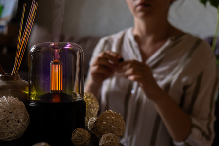Female hands adding essential oil to Close up of home perfume scent air humidifier with light....