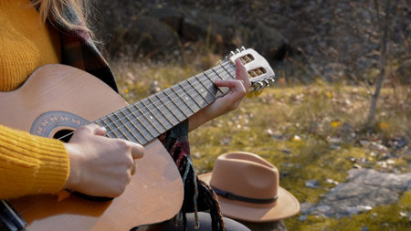 Close up of hands artist plays wooden acoustic guitar in autumnal park. Young songwriter plays string musical instrument hobby outside in nature fall time. Audio music healingの写真素材