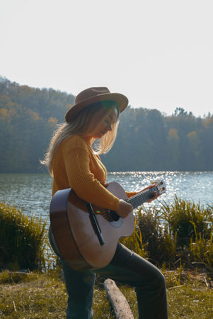 Portrait of smiling caucasian artist plays wooden acoustic guitar in autumnal park. Young songwriter...