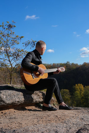 Blonde man playing acoustic guitar and singing outdoors on sunny autumn day. Artist learning and practicing playing musical instrument. Fall leaves autumnalの写真素材
