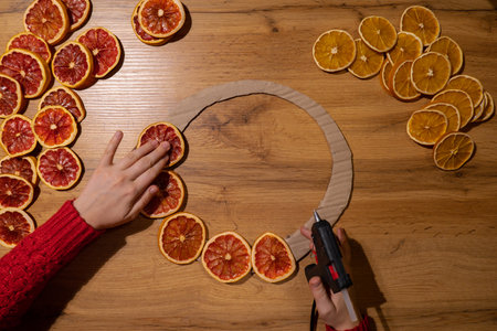 Woman using hot glue Handmade Christmas wreath from dried orange grapefruit slices. Festive holiday...