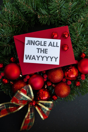 JINGLE ALL THE WAY text on postcard with red envelope on handmade Christmas wreath. Zero waste...